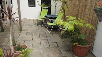 Un patio con suelo de piedra, sillas verdes, una mesa y plantas en macetas.