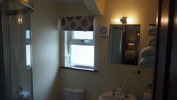 A bathroom with a shower, toilet, sink, and a window with patterned curtains.