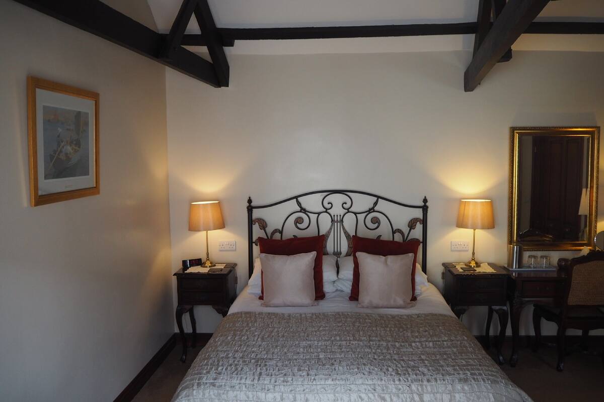 A bedroom with a large bed, two bedside tables, a mirror, and a framed picture on the wall.
