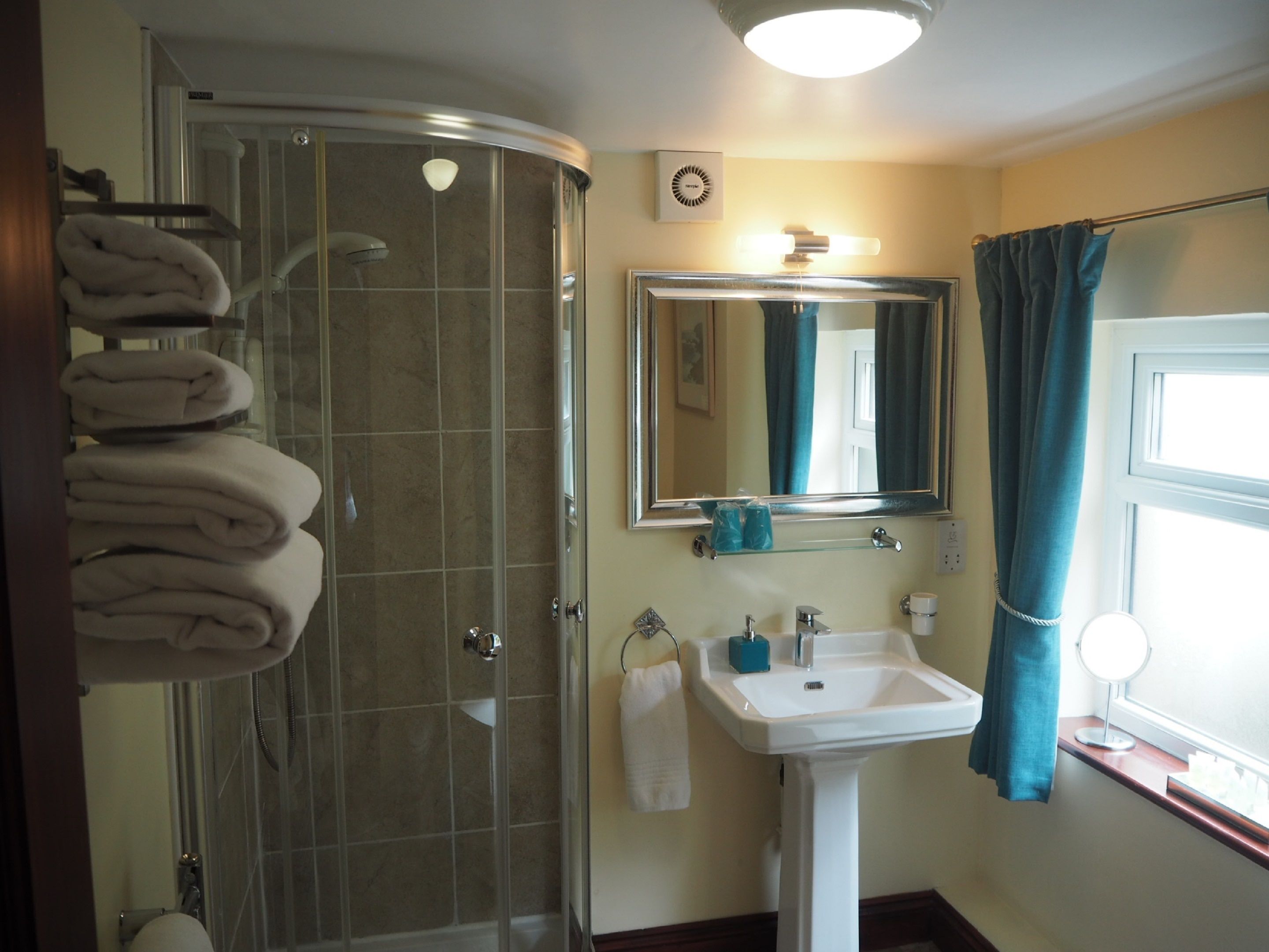 A bathroom with a glass-enclosed shower, a white sink, a mirror, and towels stacked on a rack.