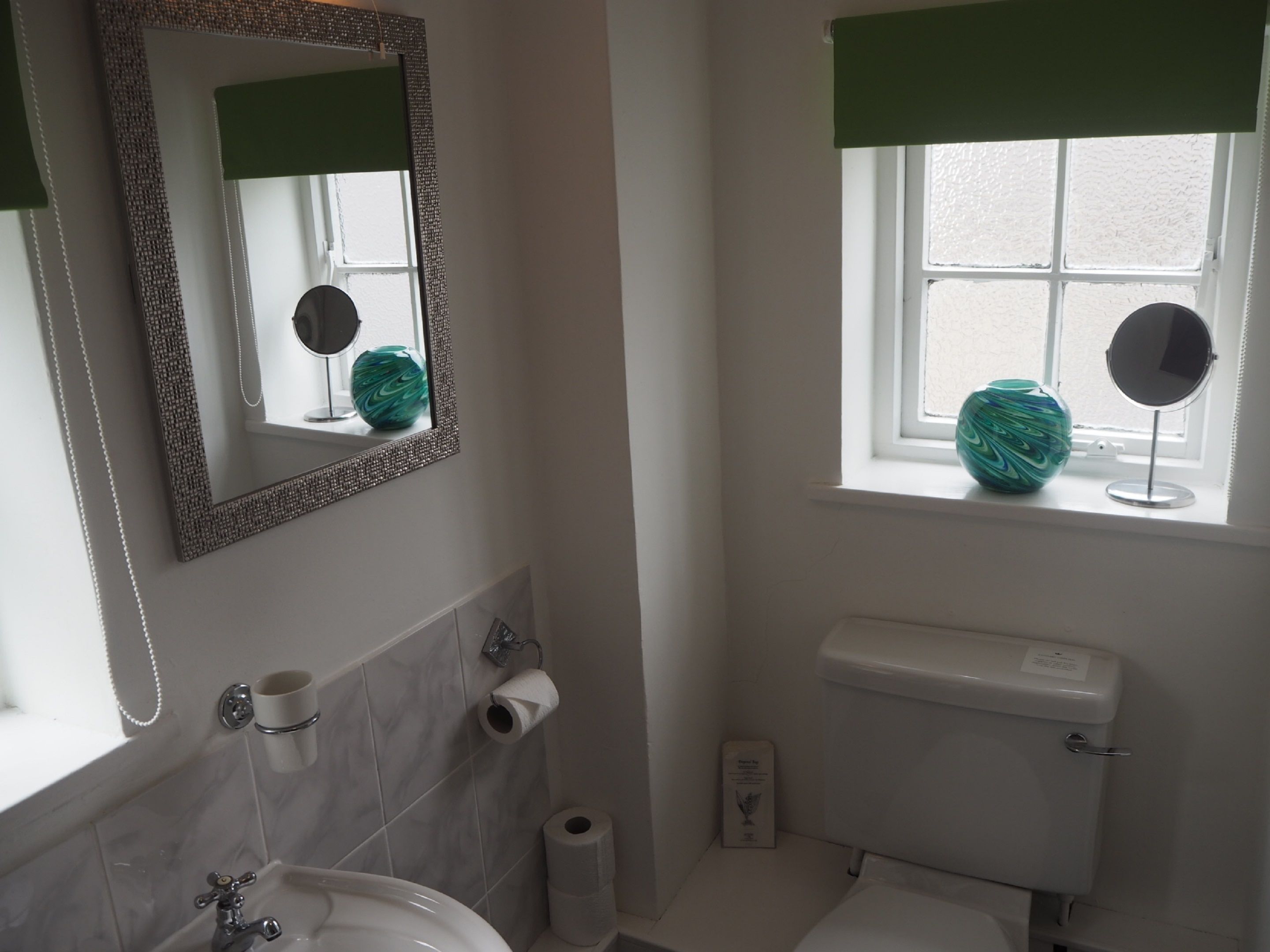 A bathroom with a sink, toilet, and a window with a vase.