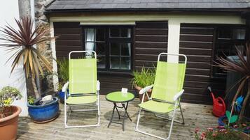 A wooden house with two green chairs and a small table on a wooden deck.