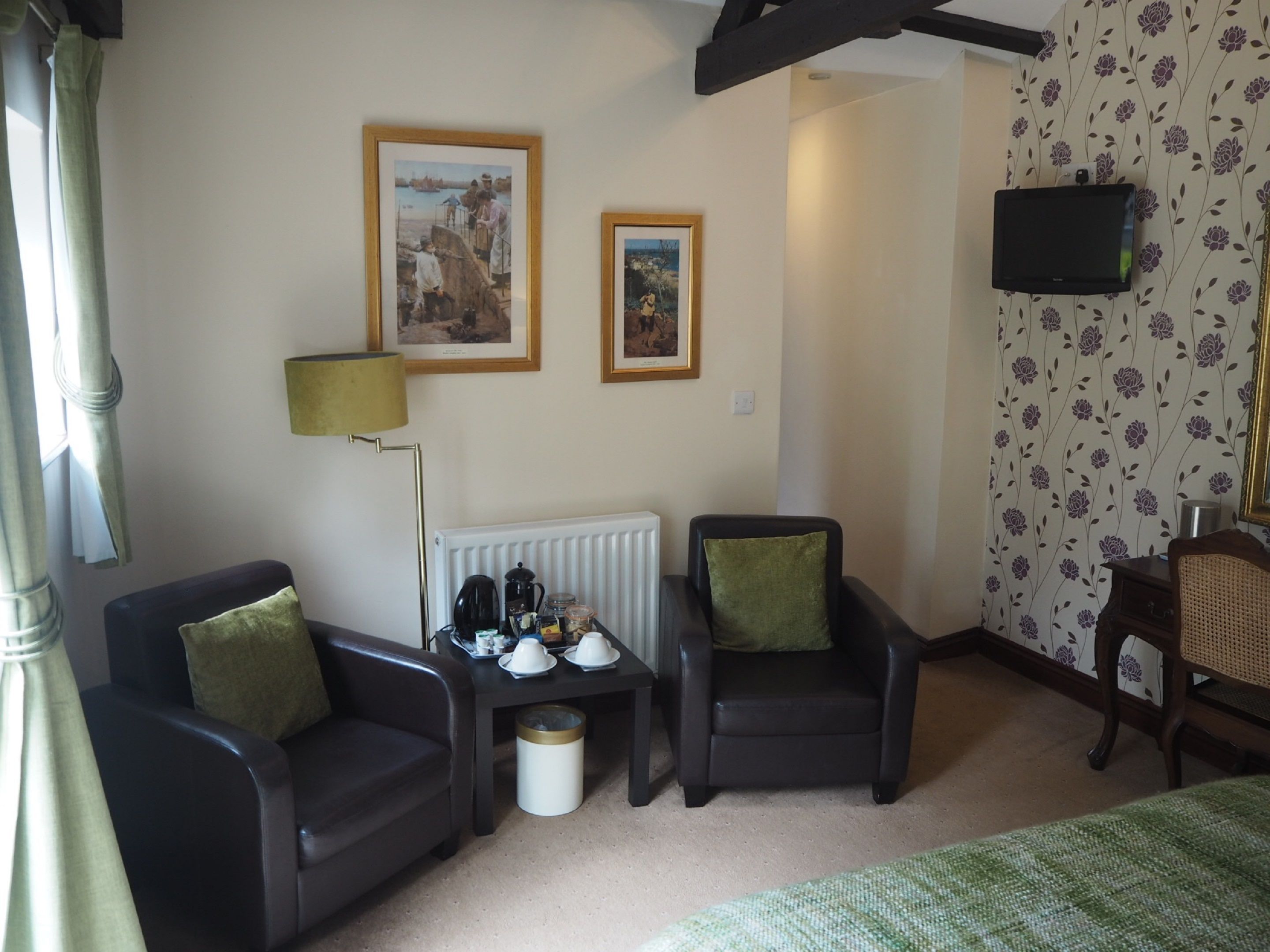 Une pièce comprenant deux fauteuils, une petite table avec une lampe, un radiateur et deux tableaux encadrés accrochés au mur.
