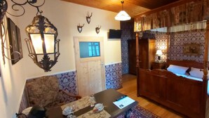 Una habitación con una cama matrimonial con dosel de madera, una mesa de comedor con sillas, una araña y apliques decorativos en la pared.