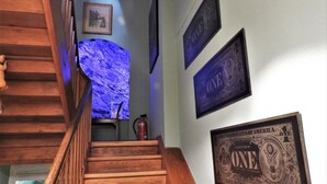 Una escalera de madera con un elemento de luz azul, un cuadro enmarcado en la pared y tres marcos con billetes de 'ONE DOLLAR'.
