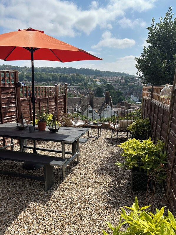 A patio with a table and chairs, a red umbrella, and a view of a town.