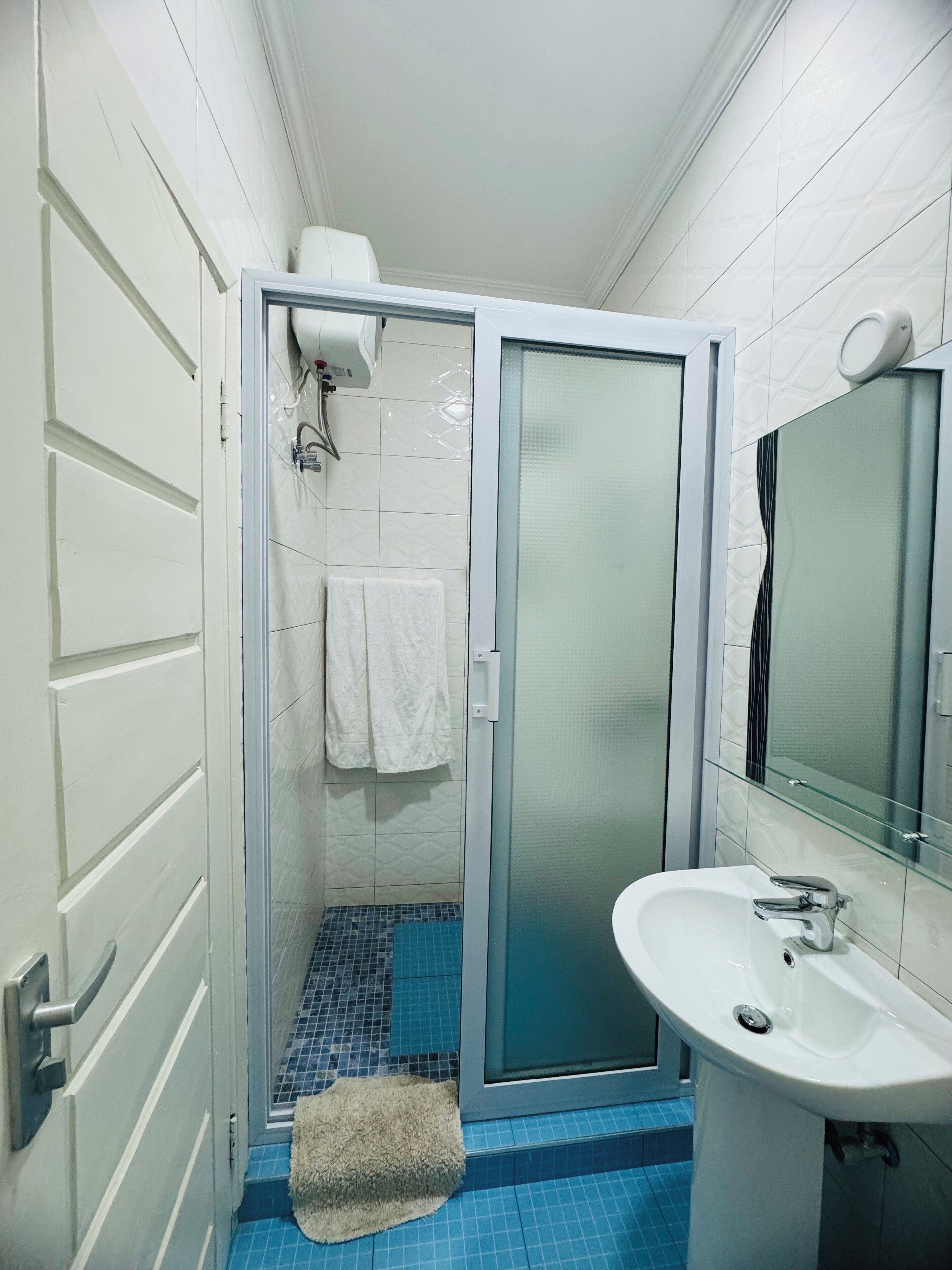 Une salle de bain avec une porte de douche en verre, un lavabo blanc et une serviette accrochée au mur.