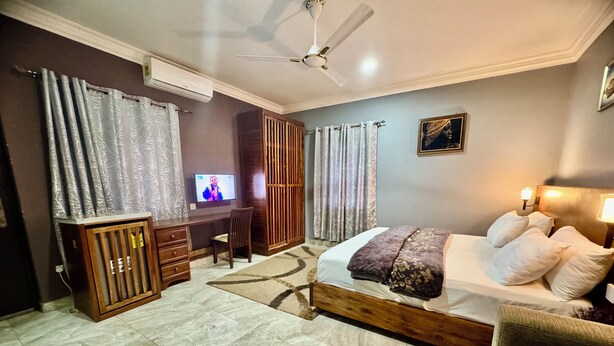 A bedroom with a bed, a TV, a wardrobe, and a desk. - Dafika Lodge (Tema)