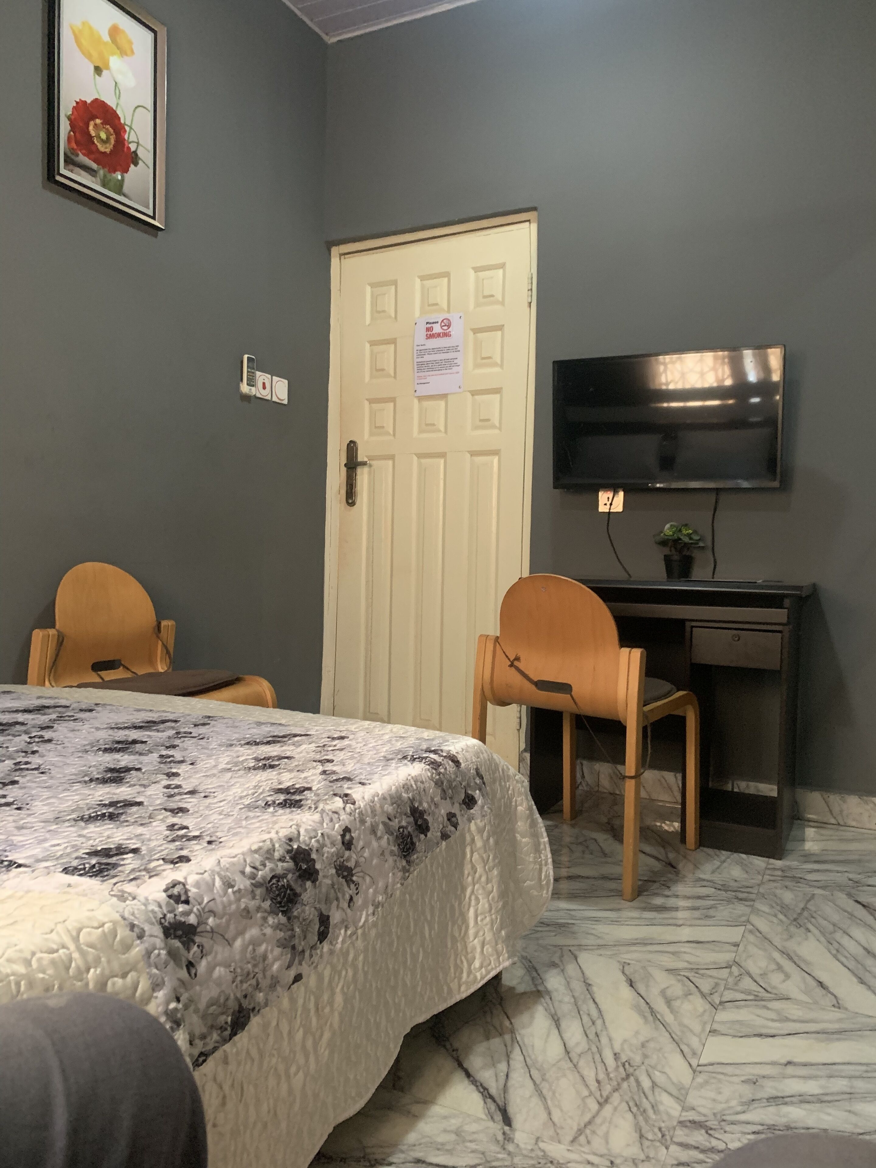 Une chambre à coucher avec un lit, deux chaises, un bureau avec une télévision, une porte sur laquelle est apposée une pancarte « Il est interdit de fumer » et un téléphone fixé au mur.