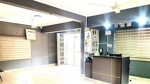 A reception area with a reception desk, a ceiling fan, and a large window with blinds. - Dafika Lodge (Tema)