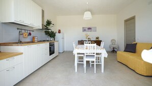 Une cuisine compacte avec des meubles blancs, une table à manger avec des chaises et un canapé jaune dans un salon lumineux.