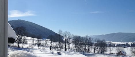 A snowy landscape with icicles hanging from a roof, a clear blue sky, and a distant view of mountains.