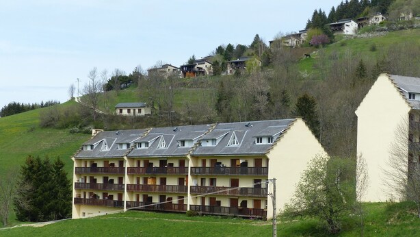 Ein mehrstöckiges Hotel mit Balkonen, gelegen auf einer grünen Hügelkuppe, mit weiteren Gebäuden im Hintergrund.
