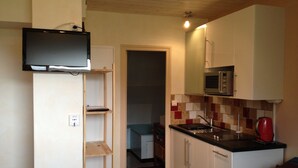 Eine kleine Küche mit einer Mikrowelle, einem Spülbecken und einem an der Wand befestigten Fernseher.