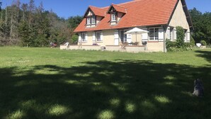 Ein zweistöckiges Haus mit rotem Ziegeldach, einer überdachten Terrasse mit Gartenmöbeln und einem gepflegten Rasen.