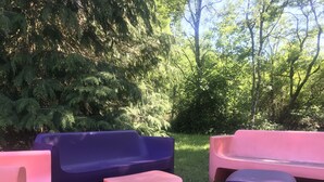 Sitzgelegenheiten im Freien mit einer Rasenfläche und dichter Bepflanzung im Hintergrund.