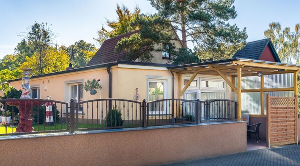 Un bâtiment à la façade beige, doté d’un toit rouge et d’une pergola en bois.