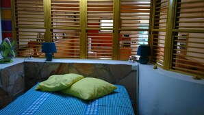 Une chambre avec un lit, un ventilateur, une lampe et une fenêtre avec des stores.