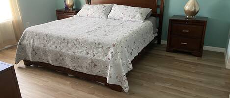 A bedroom with a wooden bed, floral bedspread, two nightstands with lamps, and a dresser.