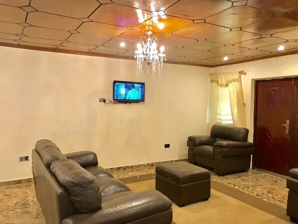 Una sala moderna con un sofá de cuero, un reposapiés y un sillón, un televisor montado en la pared y una araña.