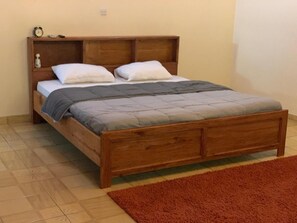 A wooden bed with a headboard, a nightstand with a clock, and a red rug on the floor.