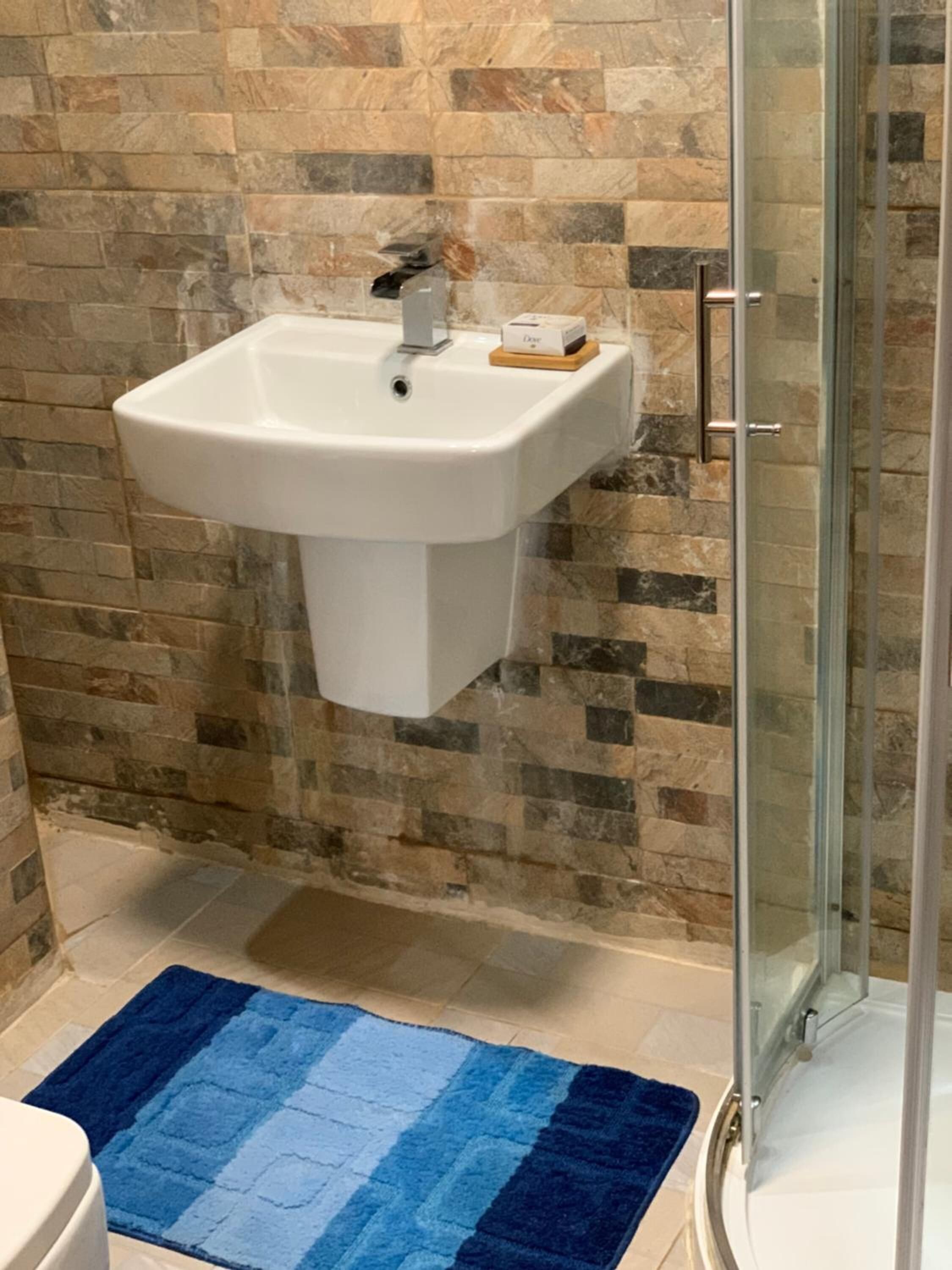 A bathroom with a white sink, a glass shower enclosure, and a blue patterned rug.