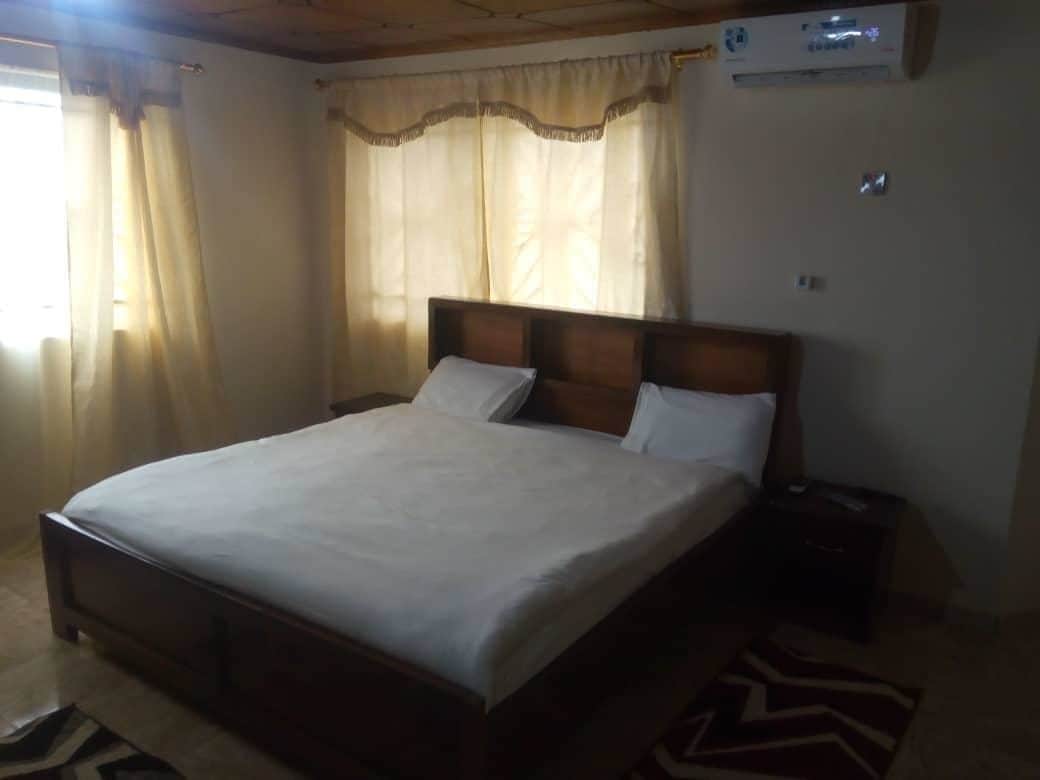 A bedroom with a wooden bed, white bedding, a nightstand, and a wall-mounted air conditioner.