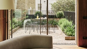 A modern room with a large sliding glass door leading to a courtyard with outdoor furniture and plants. - Weymouth Mews (London)