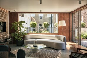 A modern living room with a sofa, a glass coffee table, a potted plant, and a view of the outside. - Weymouth Mews (London)