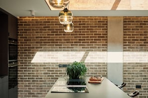 A kitchen with a brick wall, a modern light fixture, a plant, and a loaf of bread on the counter. - Weymouth Mews (London)