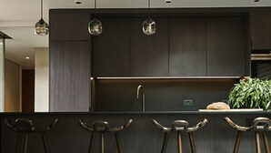 A modern kitchen with dark cabinetry, a central island with stools, pendant lighting, and a plant on the island. - Weymouth Mews (London)