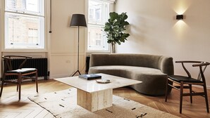 A modern living room with a sofa, two chairs, a coffee table, a floor lamp, and a large plant. - Weymouth Mews (London)