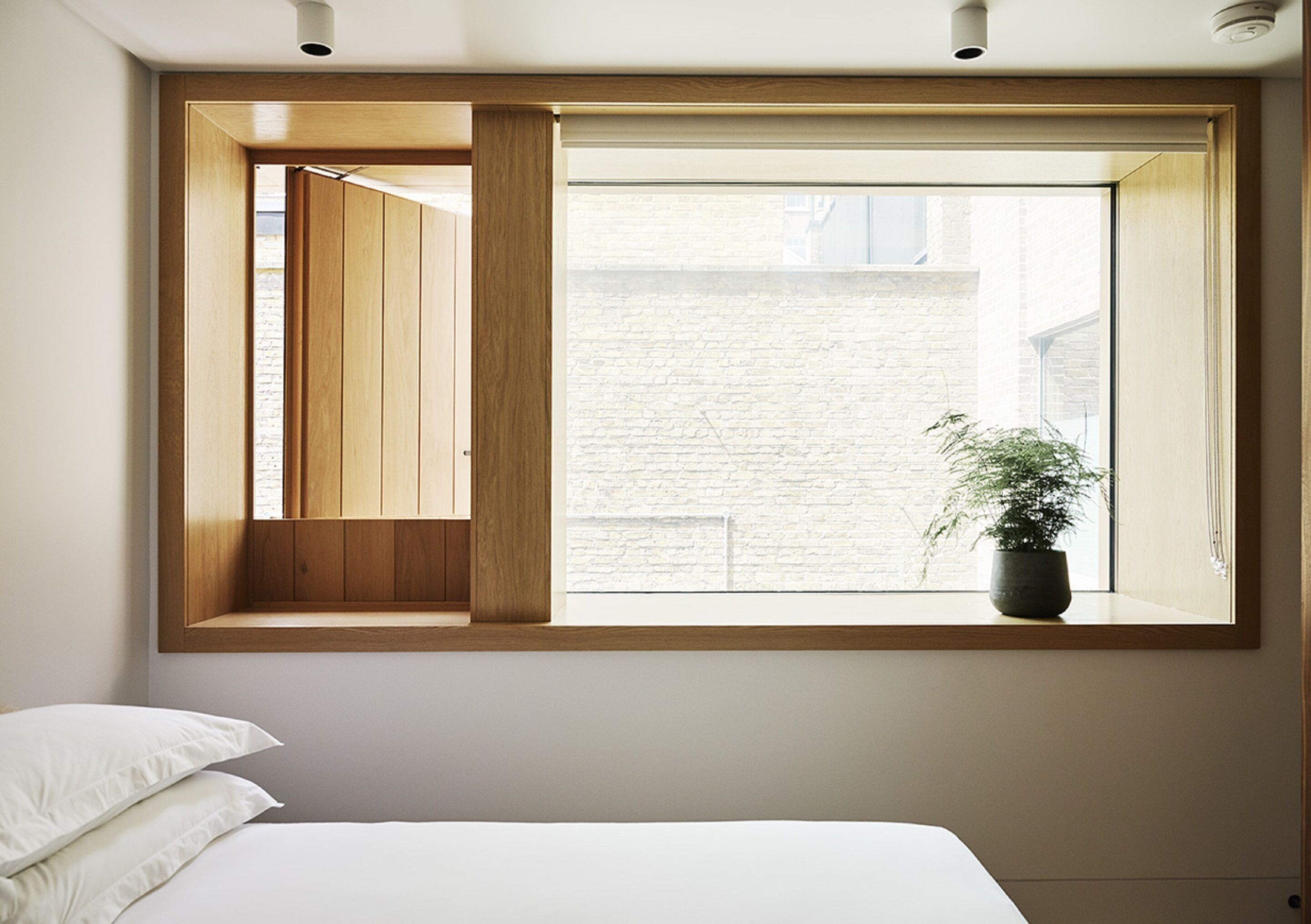 A bedroom with a large window, a bed, and a potted plant.