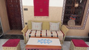 A room with a woven sofa, two matching poufs, and a central wooden table with intricate patterns. - Chambres d'Hôtes Riad Dar Tazoulte (Agdz)