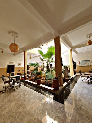 Un espacio interior amplio con un jardín central, arreglos de asientos y un techo con detalles decorativos.