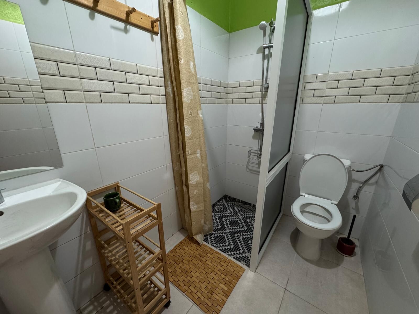Un baño con ducha, inodoro, lavabo y un estante de madera con una taza.