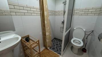 Un baño con ducha, inodoro, lavabo y un estante de madera con una taza.