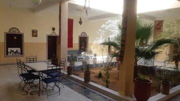 Un espacio interior amplio con suelo de baldosas, una mesa de comedor con sillas y varias plantas en macetas.