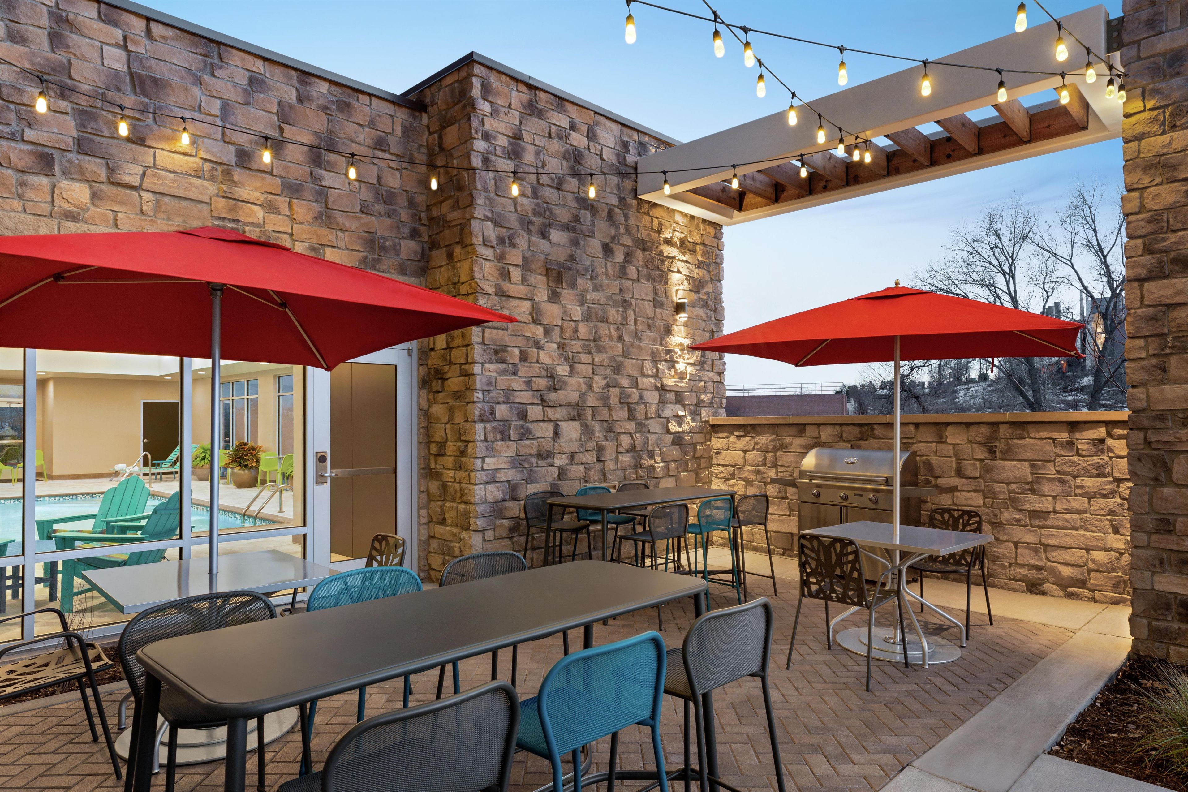 Eine Terrasse im Freien mit Steinmauern, Lichterketten und roten Sonnenschirmen.