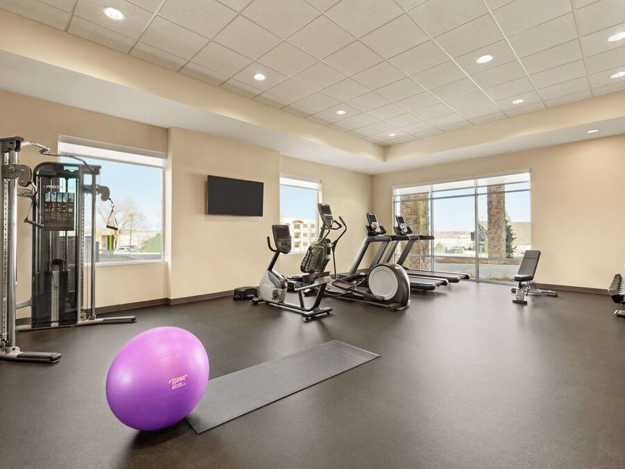 Uma academia com equipamentos de ginástica, uma janela grande e uma bola de exercícios roxa.