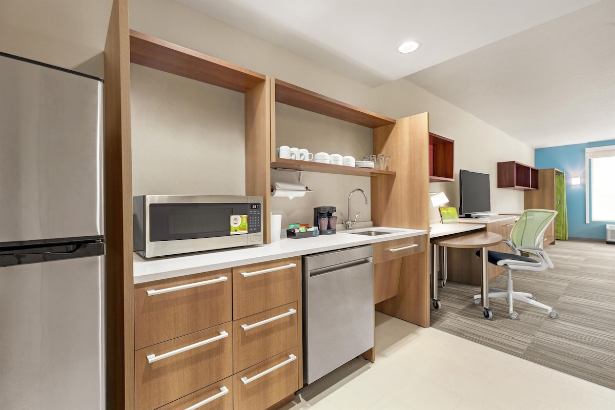 A modern kitchen with a microwave, coffee maker, and a sink. There is a wooden cabinet with drawers and a dishwasher.