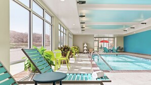 An indoor swimming pool area with lounge chairs, a table, and potted plants.