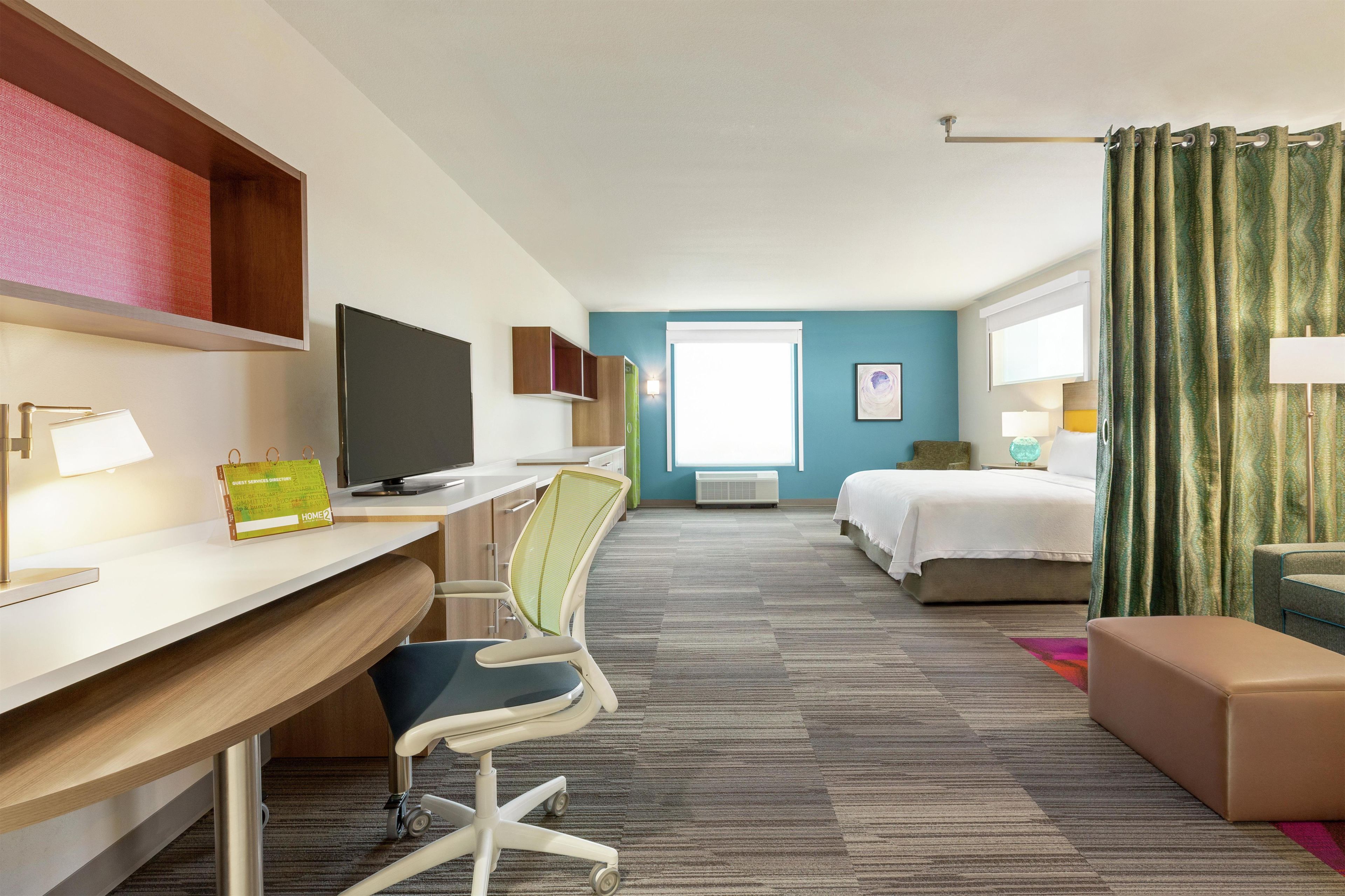 A hotel room with a desk, chair, bed, and a view of the outdoors.