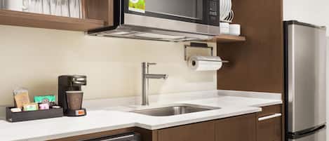 Una cocina moderna con microondas integrado, pileta de acero inoxidable y cafetera.