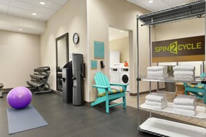 Une salle de sport équipée de matériel d’exercice, d’un distributeur d’eau, d’une horloge et d’un espace buanderie avec des serviettes.