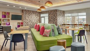 A modern interior with a green sofa, wooden tables, and chairs, a stone wall, and a large window.