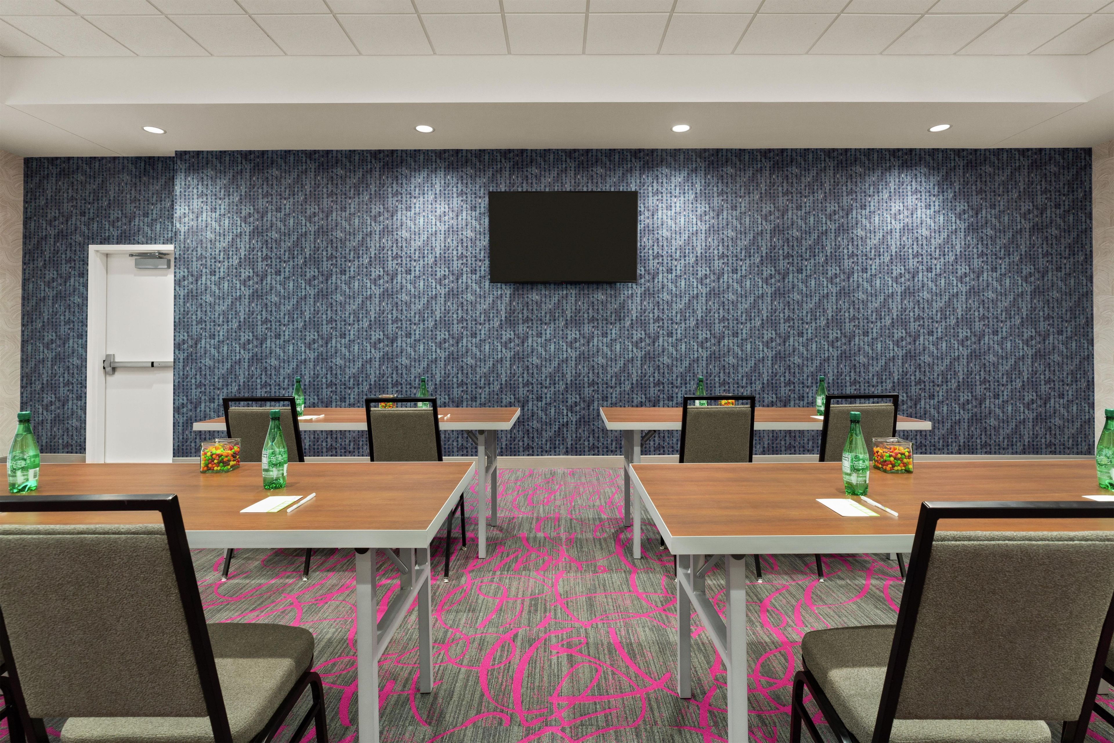A conference room with four tables, chairs, a flat-screen TV, and a refrigerator.