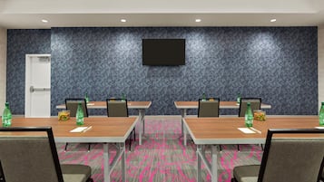 A conference room with four tables, chairs, a flat-screen TV, and a refrigerator.