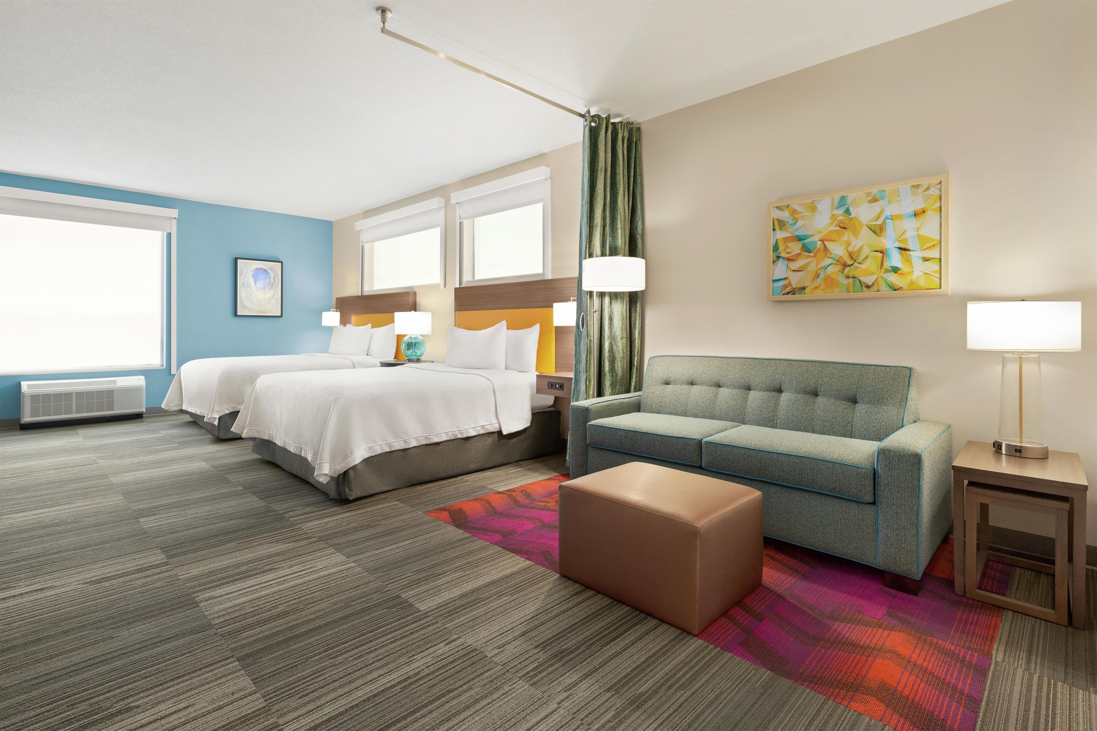 A hotel room with a bed, a sofa, a small table, a lamp, and a painting on the wall.
