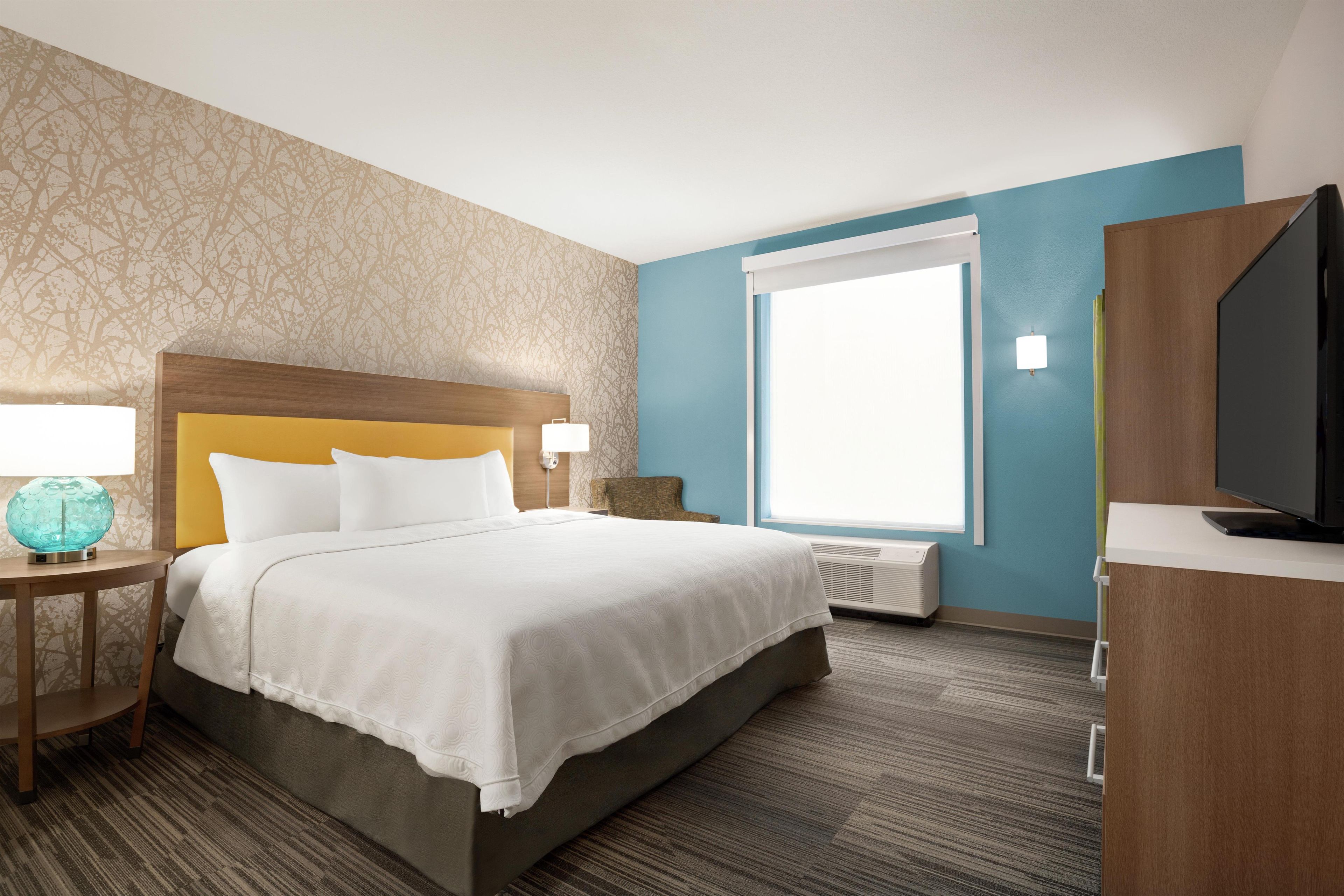 Une chambre d’hôtel avec un lit, une télévision, une fenêtre et un mur décoré d’un motif représentant un arbre.